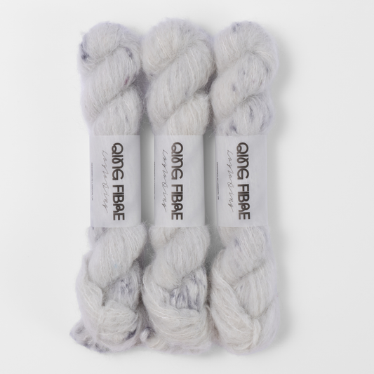 Three labelled hanks of Platinum Melted Baby Suri 25g yarn in white with grey markings.