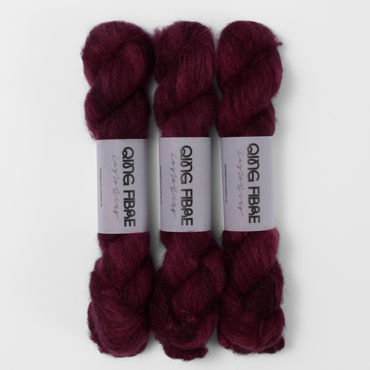 Three labelled hanks of Hush Melted Baby Suri 25g yarn in burgundy red.