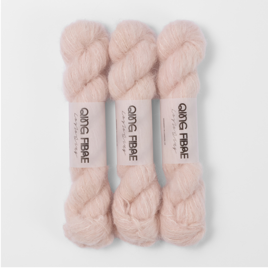 Three labelled hanks of Dust Melted Baby Suri 25g yarn in pale blush pink.
