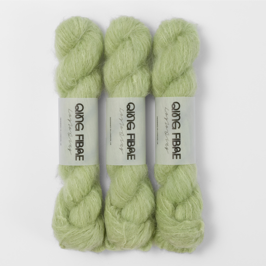 Three labelled hanks of Cicada Melted Baby Suri 25g yarn in pale sage green.