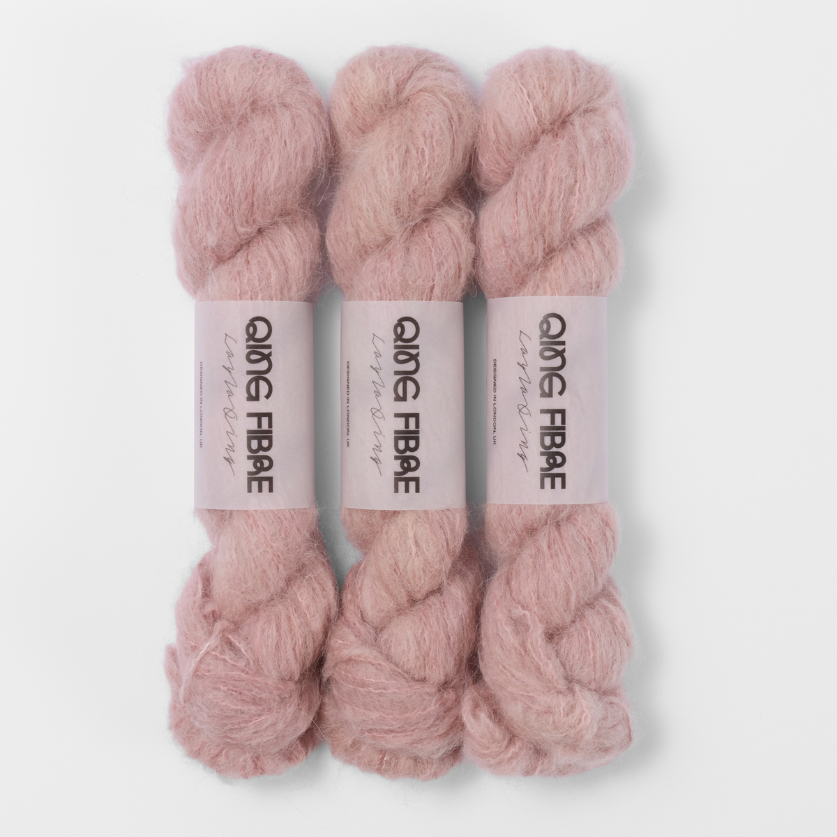 Three labelled hanks of Soft Clay Melted Baby Suri 25g yarn in dusty pink.