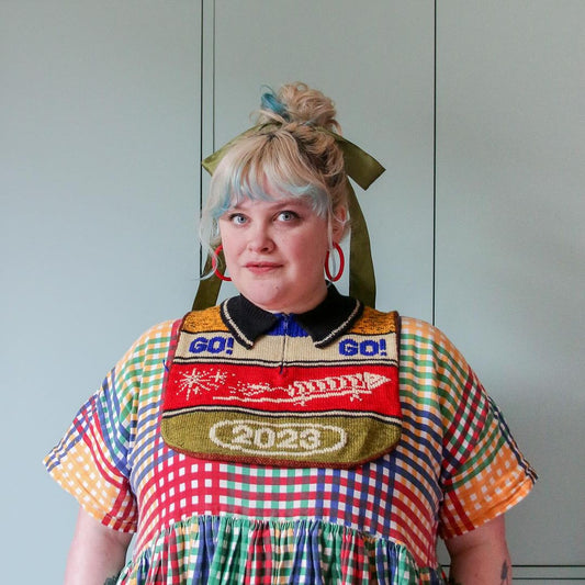 Woman with blonde hair and blue streak, wearing colorful checkered dress and bib reading 2023