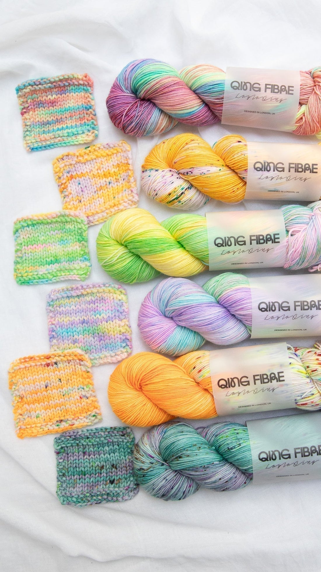 Colorful Qing Fibre yarn skeins and matching knitted swatches on a white fabric background
