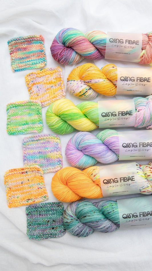 Colorful Qing Fibre yarn skeins and matching knitted swatches on a white fabric background