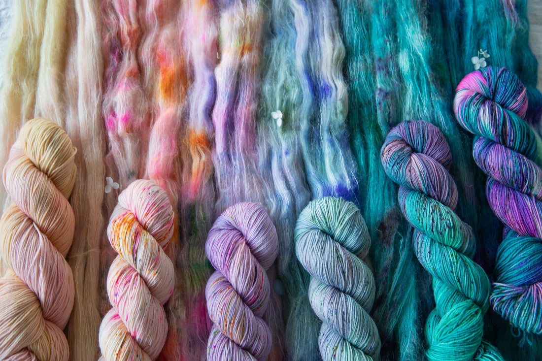 Hand-dyed colorful yarn skeins and roving in blue, purple, pink, and cream hues
