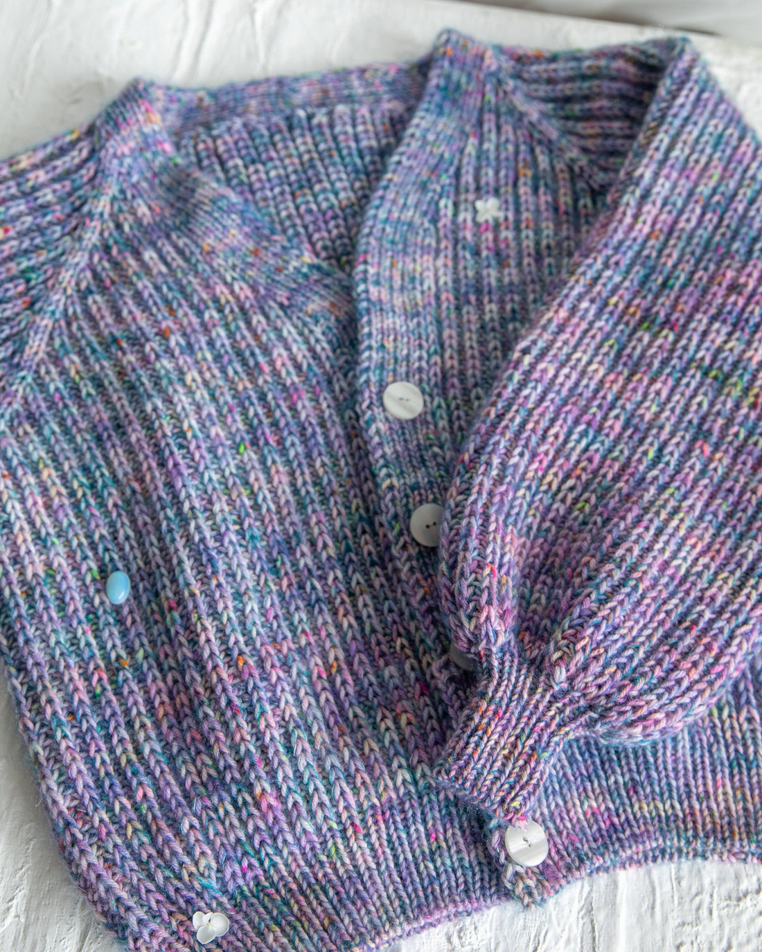 Hand-knit multicolored purple ribbed cardigan with white buttons on textured surface