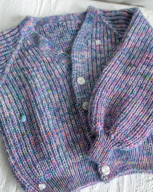 Hand-knit multicolored purple ribbed cardigan with white buttons on textured surface