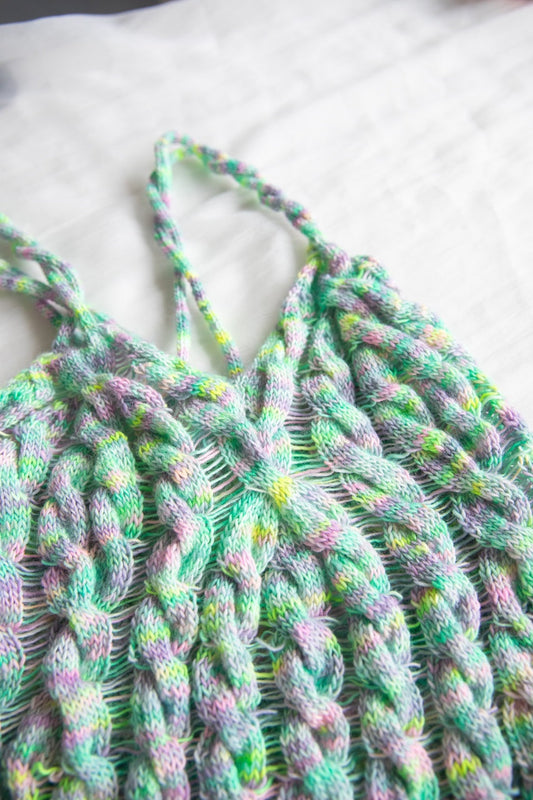 Hand-knit pastel braided top with twisted straps on white fabric background