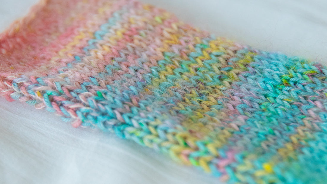 Close-up of colorful hand-knit wool fabric with pastel rainbow yarn on a white surface