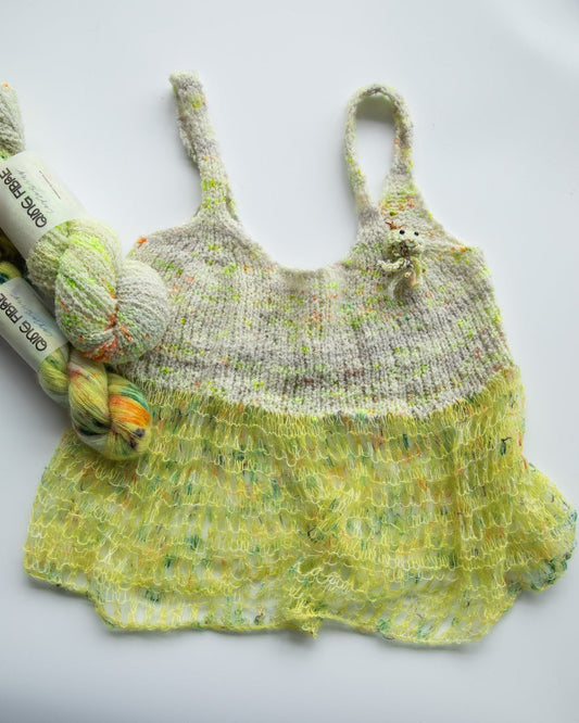 Hand-knitted yellow speckled tank top with yarn skeins on white background