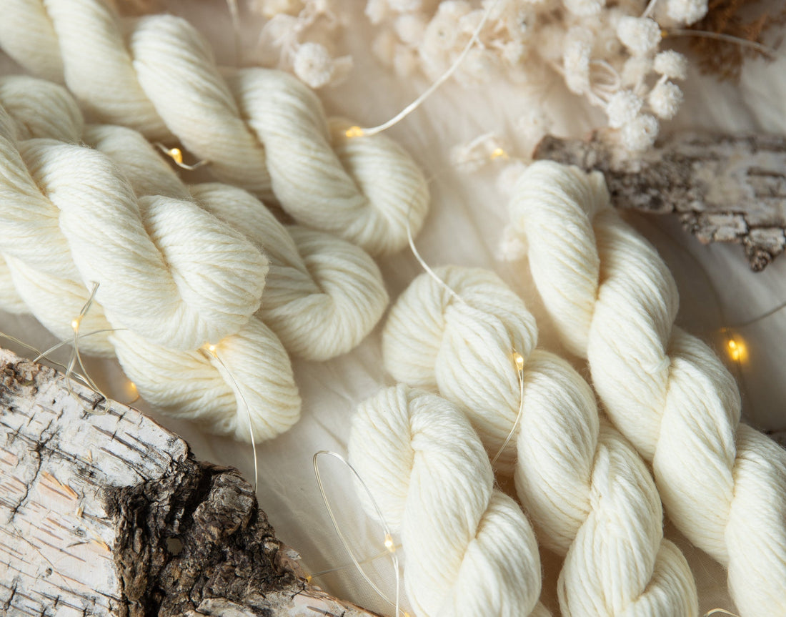 Cream-colored yarn skeins on rustic wood with lights and dried flowers