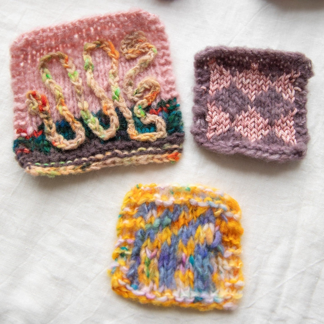 Three colorful hand-knitted swatches on white fabric background, featuring textured yarn patterns.