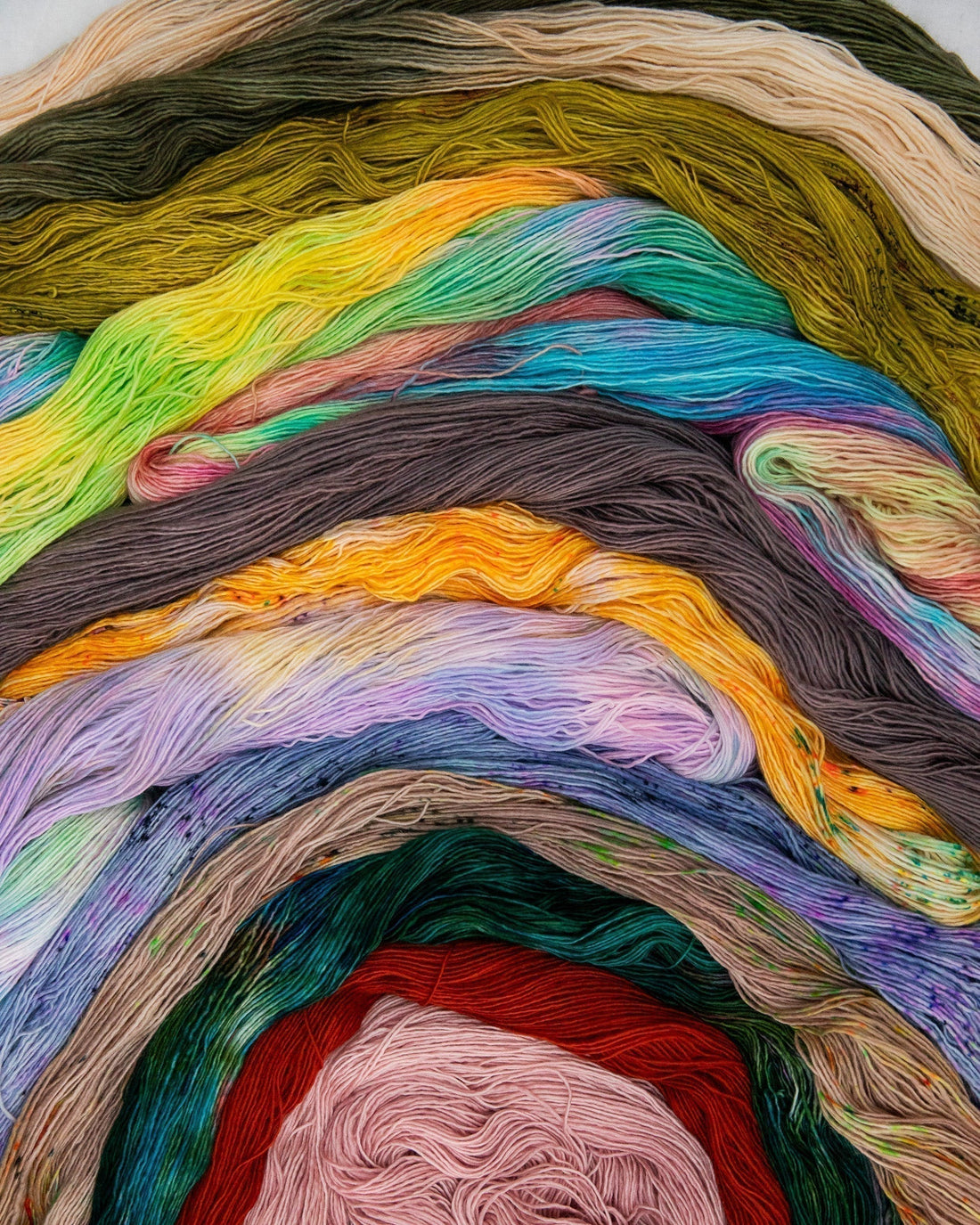 Rainbow-colored hand dyed yarn skeins arranged in layers for knitting or crochet