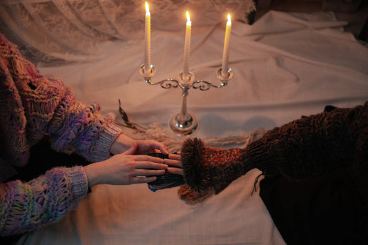 Two people in knitted sweaters holding hands by candlelight, cozy Halloween scene