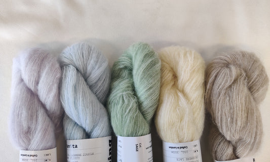 Five pastel skeins of fluffy cashmere and silk yarn on a white background