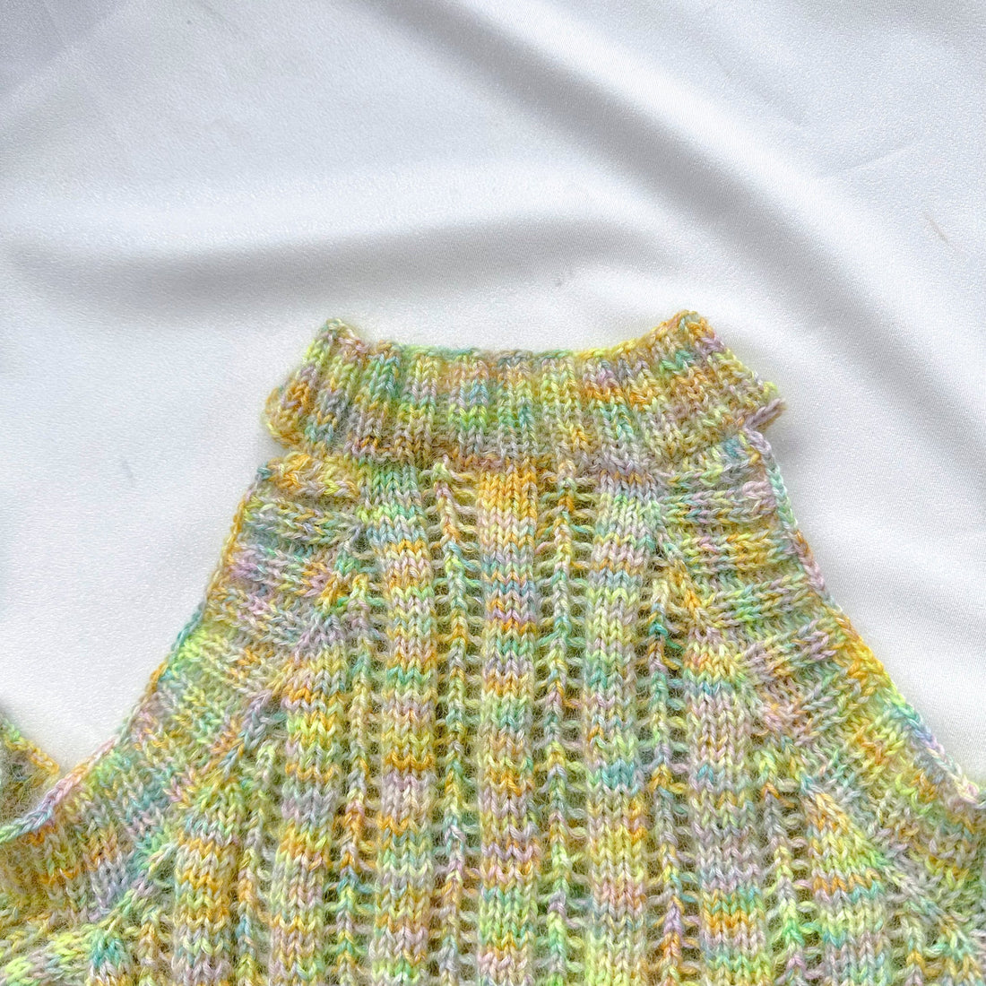 Hand-knit pastel multicolor ribbed sweater on white fabric background