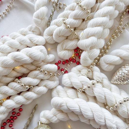 White yarn skeins with gold and red holiday beads on a festive background