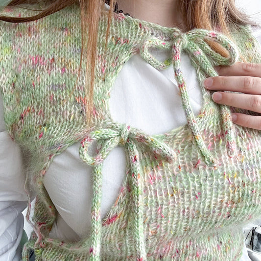 Green pastel knit vest with tie details over white shirt, close-up on upper body