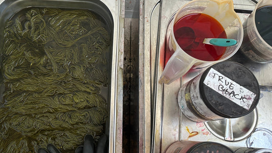 Yarn soaking in dye bath beside containers of dye and black pigment on a metal table