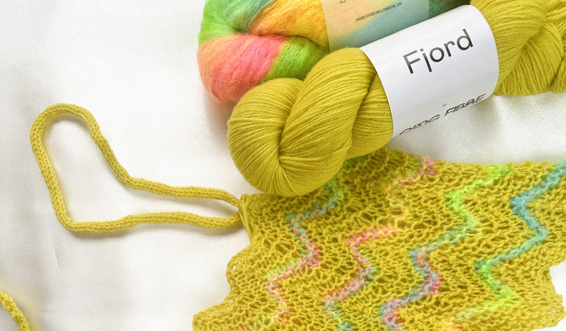 Colorful yarn skeins and knitted yellow fabric with wavy pastel stripes on white background
