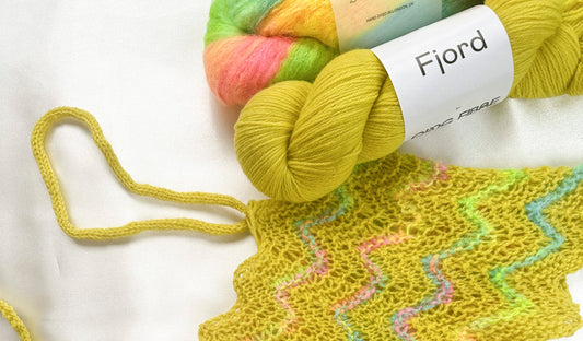 Colorful yarn skeins and knitted yellow fabric with wavy pastel stripes on white background