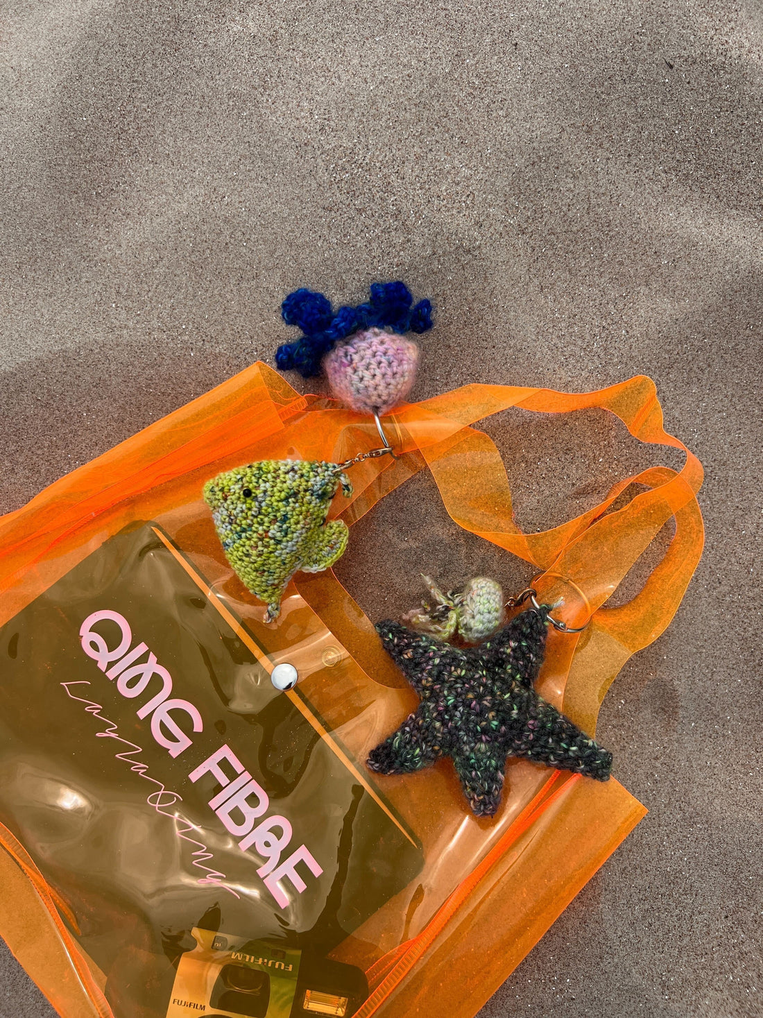 Orange transparent beach bag with crocheted sea animal keychains on sand
