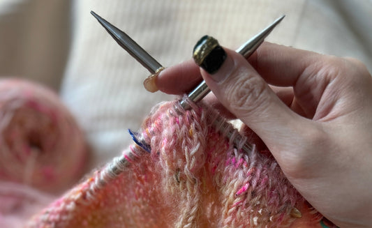 Close-up of hands knitting with metal needles and pink variegated yarn