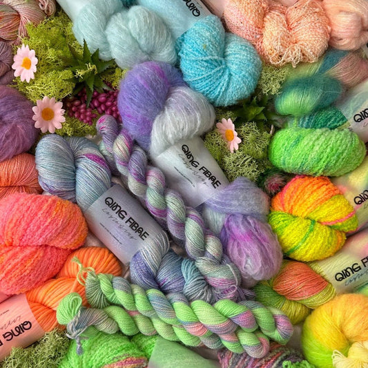 Colorful QING FIBRE yarn skeins with flowers and greenery, knitting supplies display