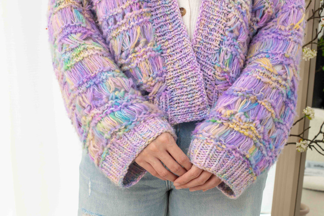 Close-up of pastel chunky knit cardigan with multicolored yarn, worn with light denim jeans