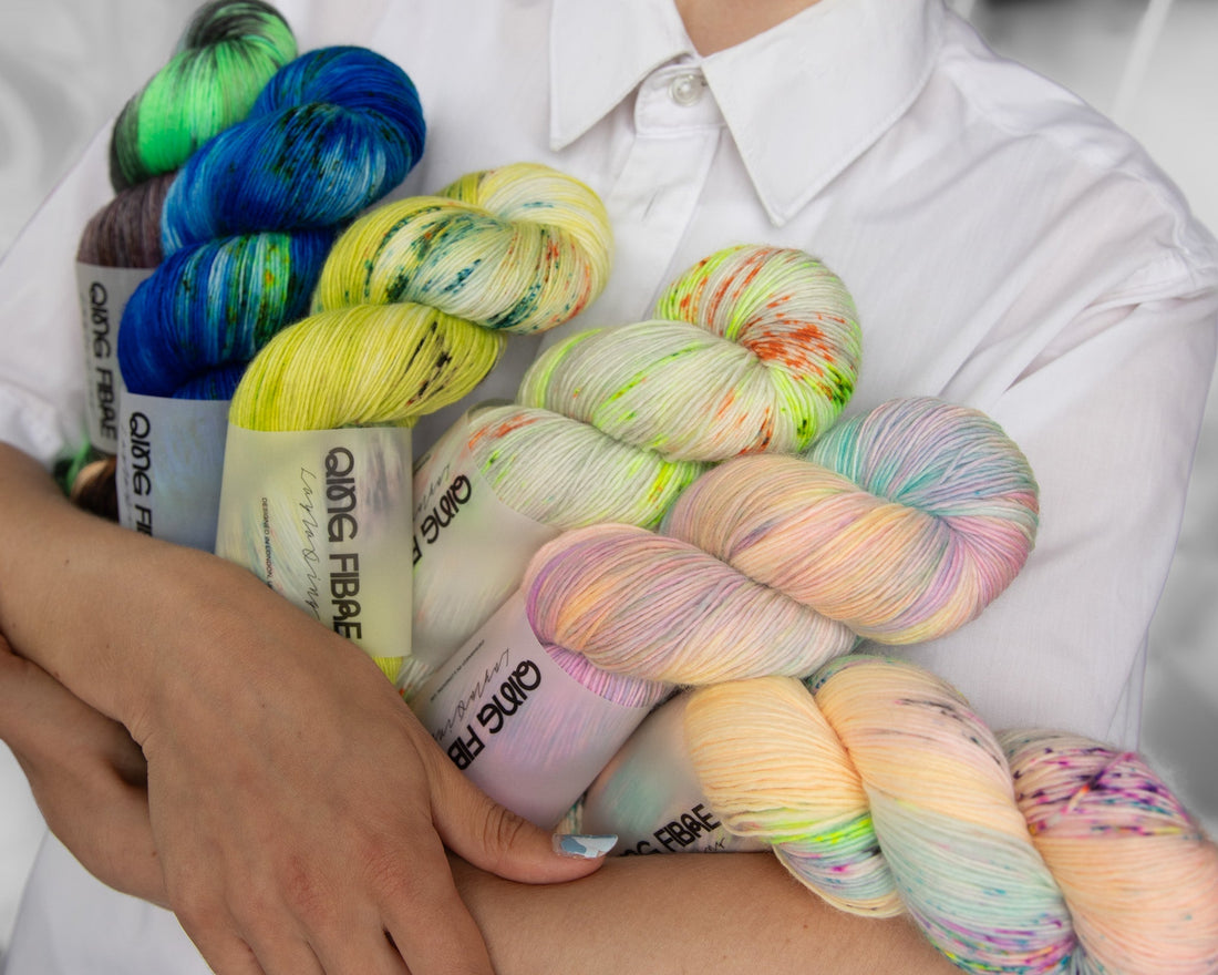 Person holding colorful hand-dyed yarn skeins in white shirt, yarn shop product photo