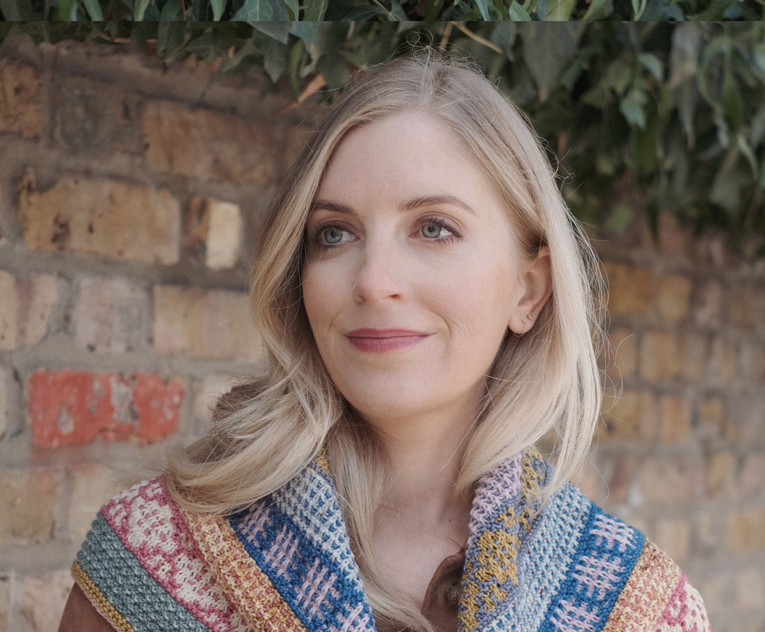 Woman with blonde hair wearing colorful knit scarf by brick wall outdoors