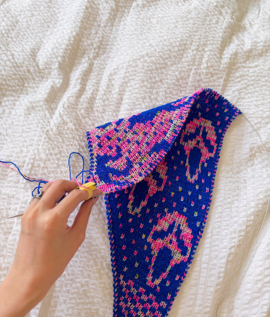a hand holding a work in progress double knit scarf, showcasing how the two sides of the scarf are not mirroring each other. the scarf is knit in hand-dyed yarn in cobalt blue and bright pink.