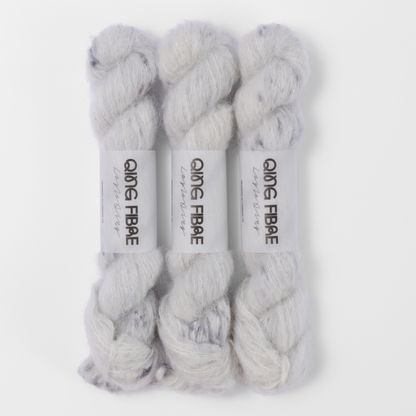 Three labelled hanks of Platinum Melted Baby Suri 25g yarn in white with grey markings.