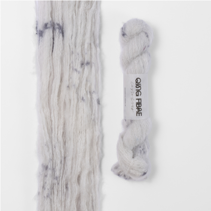 Platinum Melted Baby Suri 25g: white with grey markings yarn, shown loose beside a labelled hank.