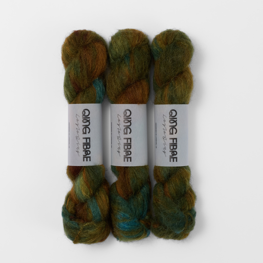 Three labelled hanks of Nyx Melted Baby Suri 25g yarn in dark green and brown.