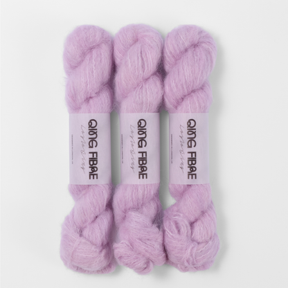 Three labelled hanks of Thistle Melted Baby Suri 25g yarn in pale lilac.