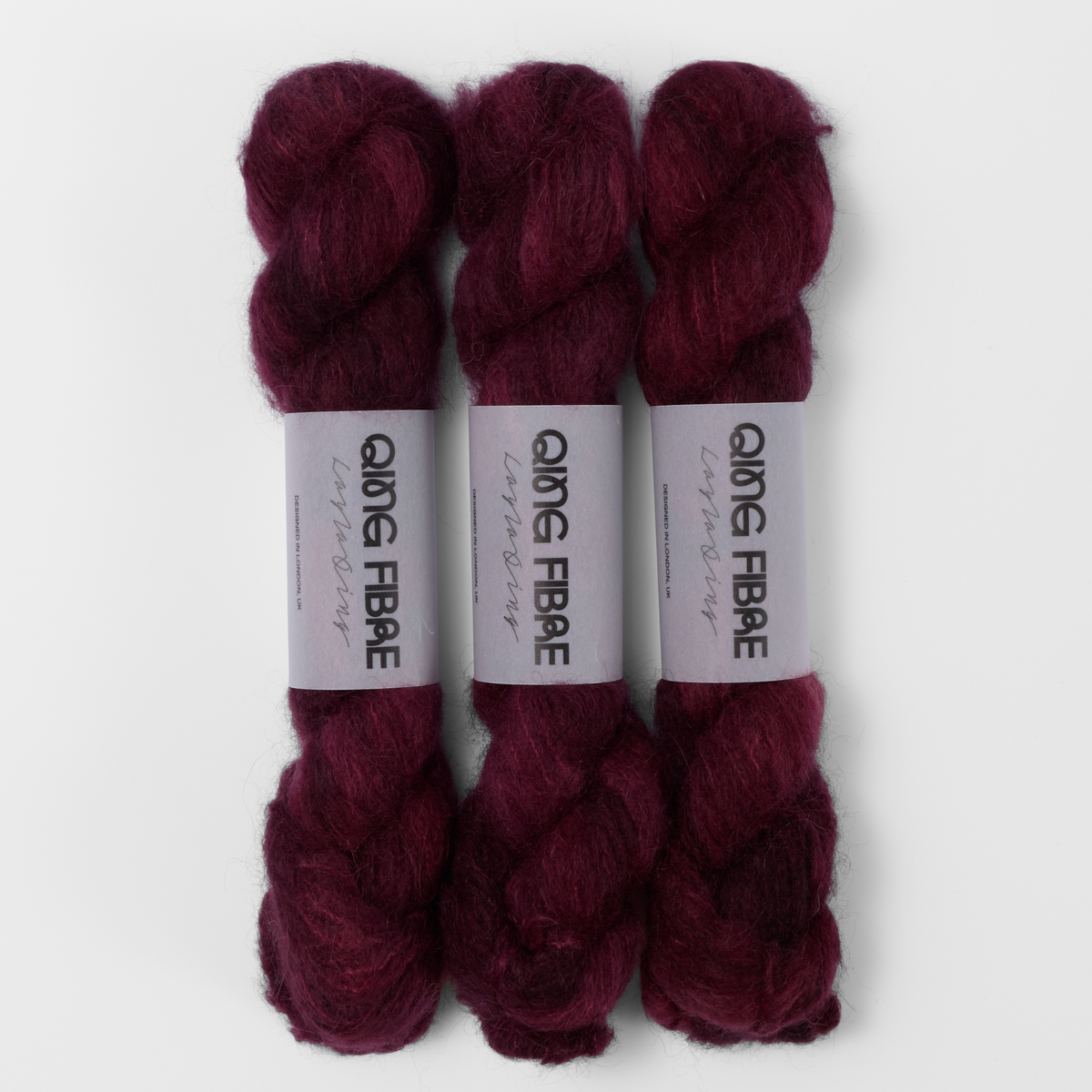 Three labelled hanks of Hush Melted Baby Suri 25g yarn in burgundy red.