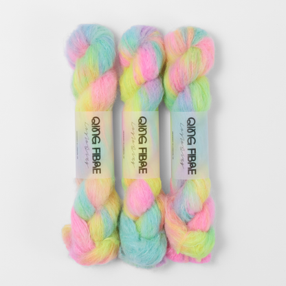 Three labelled hanks of Flying Saucer Melted Baby Suri 25g yarn in bright pink, yellow and turquoise green.