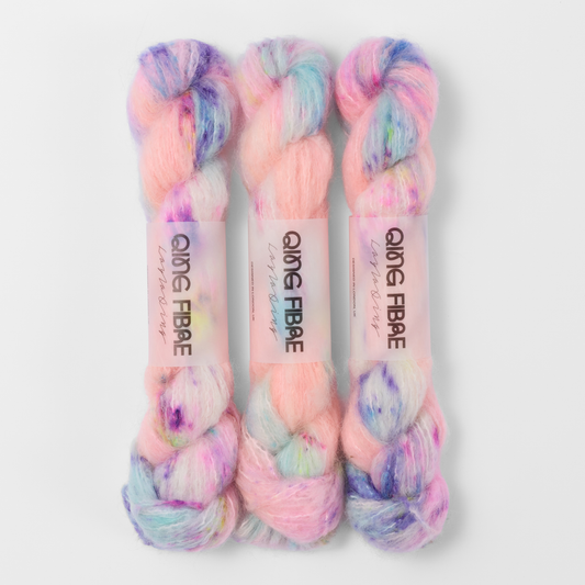 Three labelled hanks of Electric Anemone Melted Baby Suri 25g yarn in peach pink with blue and purple accents.
