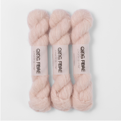 Three labelled hanks of Dust Melted Baby Suri 25g yarn in pale blush pink.