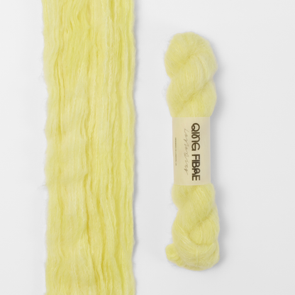Cocoon Melted Baby Suri 25g: pale yellow yarn, shown loose beside a labelled hank.