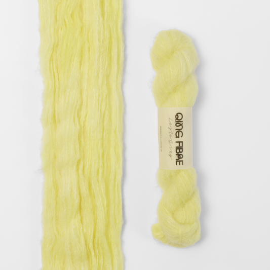 Cocoon Melted Baby Suri 25g: pale yellow yarn, shown loose beside a labelled hank.