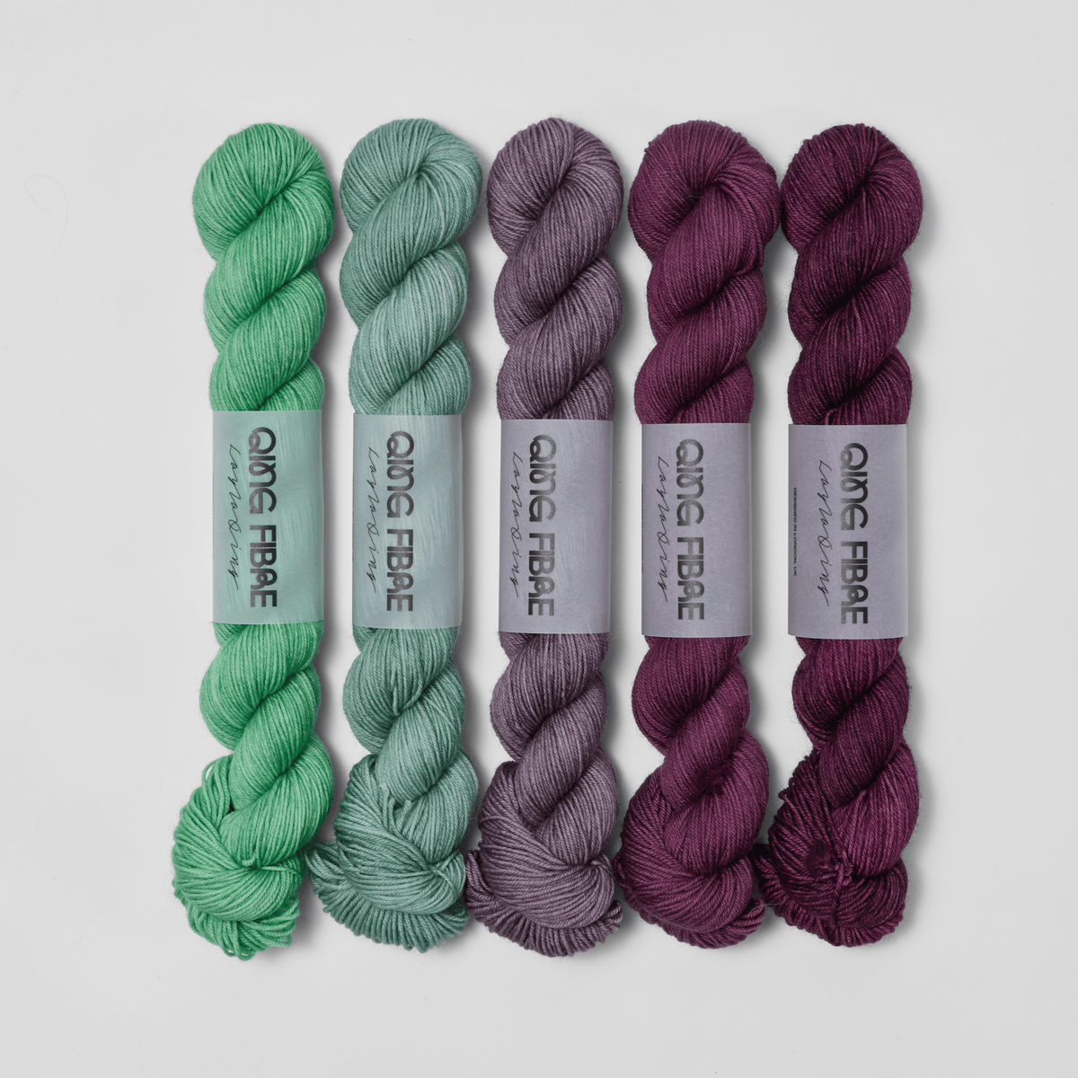 Five skeins in the Bittersweet Dashing Fingering fade set, shifting from green through grey to deep plum.