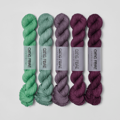 Five skeins in the Bittersweet Dashing Fingering fade set, shifting from green through grey to deep plum.