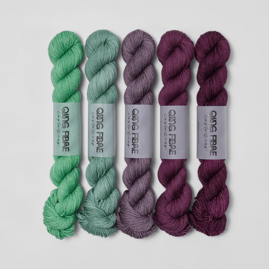 Five skeins in the Bittersweet Dashing Fingering fade set, shifting from green through grey to deep plum.