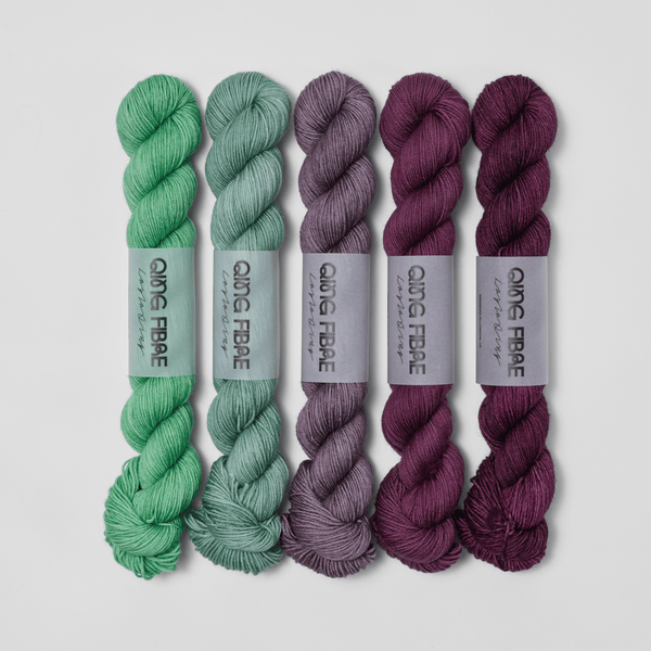 Five skeins in the Bittersweet Dashing Fingering fade set, shifting from green through grey to deep plum.