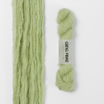 Cicada Melted Baby Suri 25g: pale sage green yarn, shown loose beside a labelled hank.