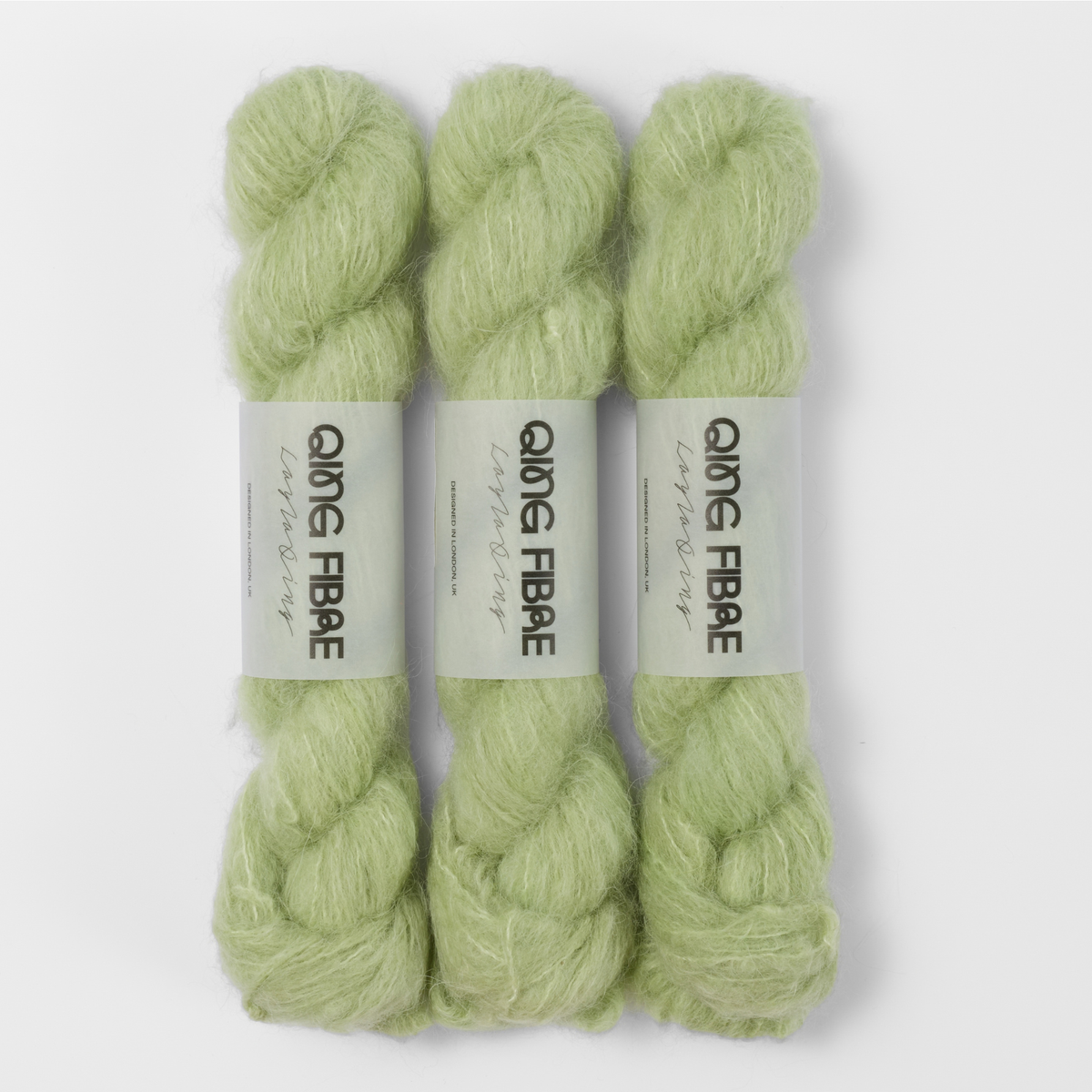 Three labelled hanks of Cicada Melted Baby Suri 25g yarn in pale sage green.