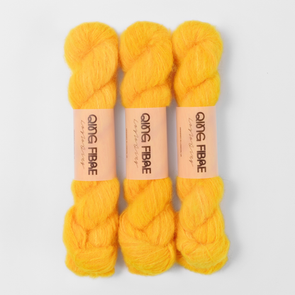 Three labelled hanks of Cheese Melted Baby Suri 25g yarn in golden orange.