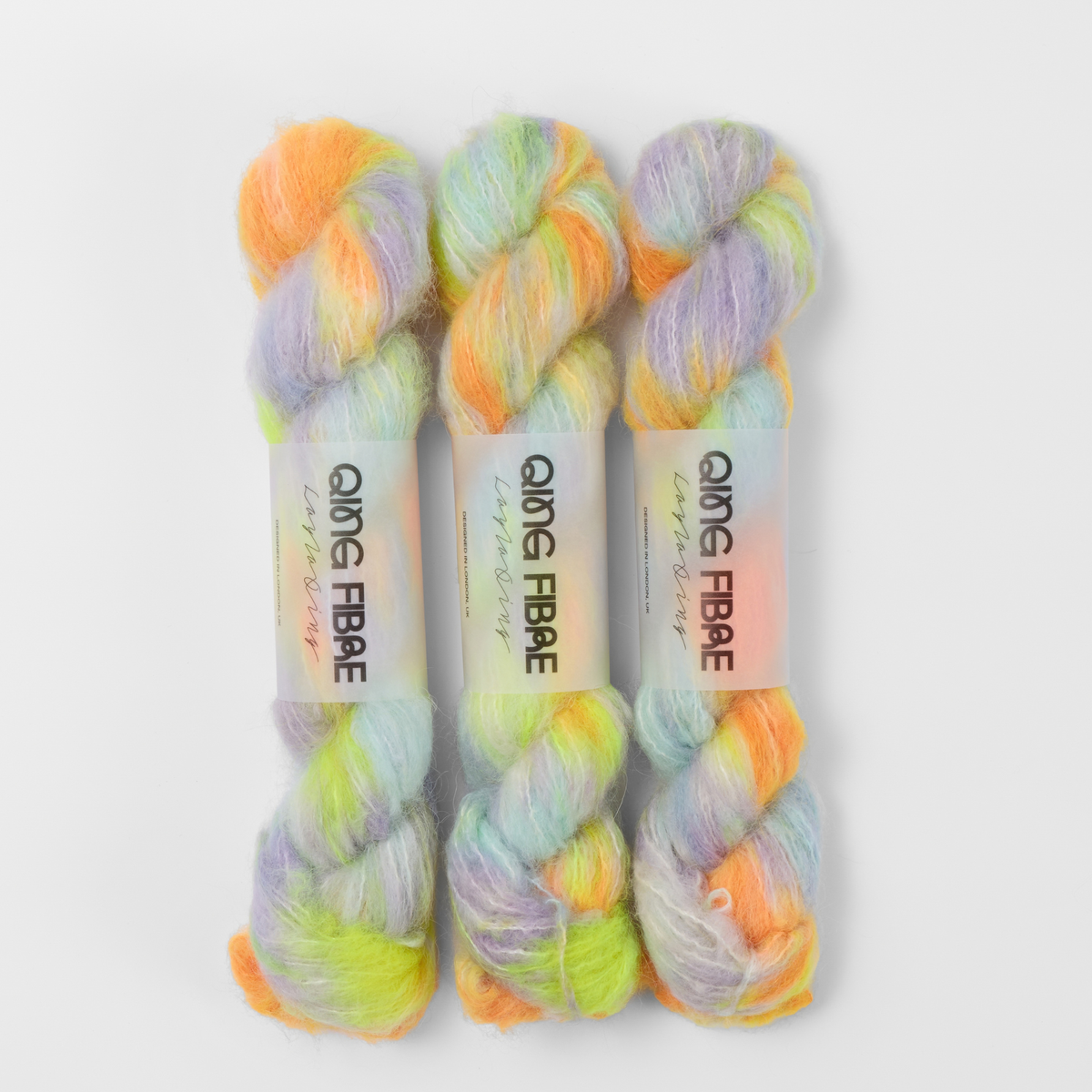 Three labelled hanks of 600 Volts Melted Baby Suri 25g yarn in yellow and orange with green and lilac.